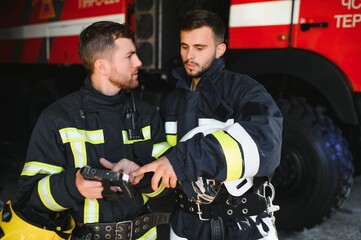 Fototapeta na wymiar Portrait of two firefighters in fire fighting operation, fireman in protective clothing and helmet using tablet computer in action fighting
