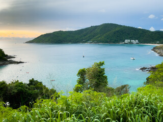 Panoramic view of Phuket coast with sailboats and people on kayaks over calm sea at sunset. Idyllic natural landscape by Promthep Cape, Thailand. Summer travel, water recreation concepts