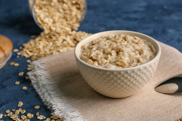 Bowl with tasty oatmeal, overturned jar and scattered flakes on blue table