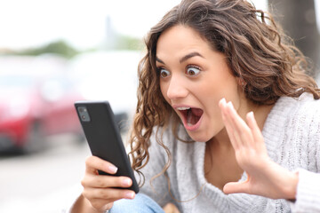 Surprised woman checking phone content in the street