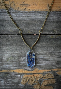 Close up pendant with small blue flowers concept photo. Craft jewelry. Top view photography with old wooden table on background. High quality picture for wallpaper, travel blog, magazine, article