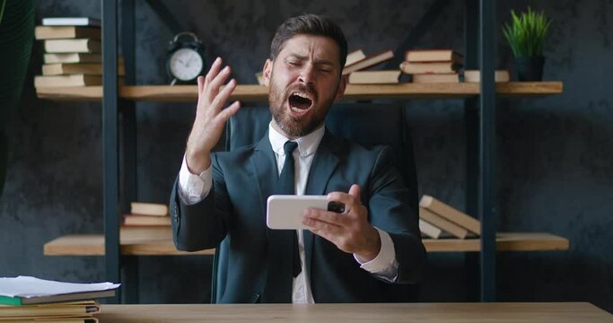 Bearded manager playing game on smartphone mobile application, disappointed failure. Manager in formal suit losing racing game on smartphone in modern office. Procrastination concept at work.