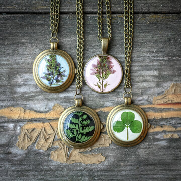 Close up pendants with wildflowers and leaves concept photo. Craft jewelry. Top view photography with old table on background. High quality picture for wallpaper, travel blog, magazine, article