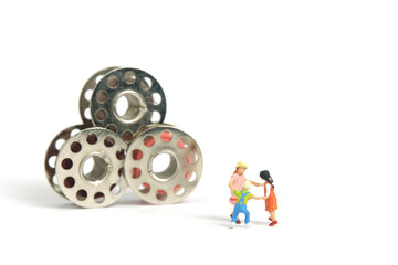 Miniature people toy figure photography. Playground arena concept. Kids playing together within sewing thread spool. Isolated on white background