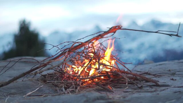 Closeup slow motion shot of bonfire in front of the snow covered mountains at Manali in Himachal Pradesh, India. Campfire in the mountain made by hiker to keep him warm during the trek in winter. 