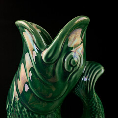 antique green ceramic vase in the shape of a fish. antique vase with an ornament on a black...