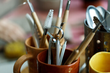 Various tools for carving pottery in mug placed on wooden table in workshop with professional instruments