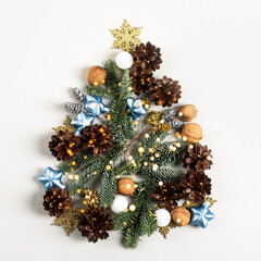 Creative Christmas composition in the shape of a Christmas tree on a gray background, consisting of pine cones, branches of a Christmas tree, ornaments, walnuts, snowflakes