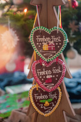 Colorful Christmas handmade gingerbread in the shape of a heart hangs on a wooden tree close-up. Christmas decor and food. Christmas cozy atmosphere. Festive fair