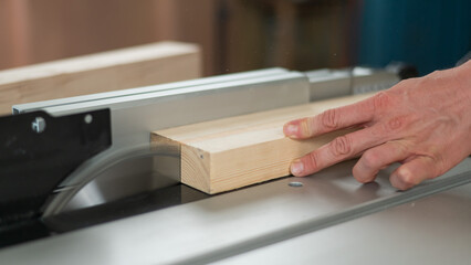 Close-up of a man cutting a wooden board on a circular machine.