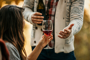 Man serving red wine to a female friend during a party at a restaurant. Millennials having an outdoor party.