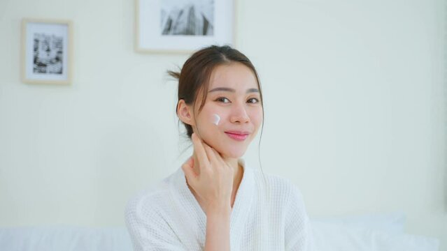 Portrait of Asian woman looking at camera after apply lotion on face.
