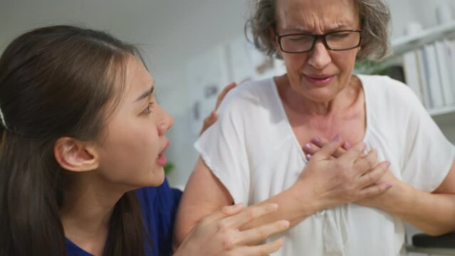 Asian caregiver saving senior woman having chest pain from heart attack.