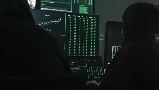 Two hackers coding to hack company servers, using monitor screens with green code