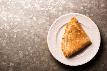 Fried thin pancake in a white plate on a metallic background