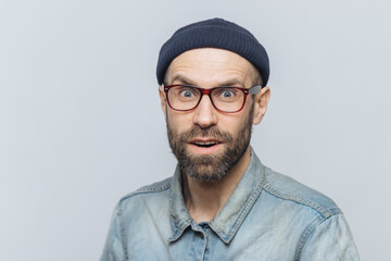 Headshot of good looking unshaven male with blue eyes, looks with suprised expression into camera,...
