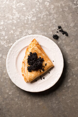 Delicious thin pancake with black caviar in a plate