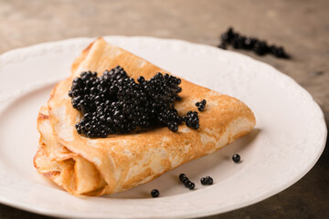 Delicious thin pancake with black caviar in a plate, close-up