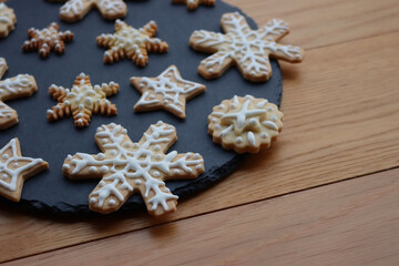 Festive gingerbread cookies in shape of Stars and Snowflakes on a black slate stone plate on wooden table