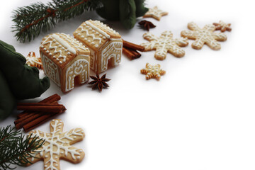 Small Gingerbread houses with many gingerbread cookies in shape of stars and snowflake  on white with pine branches, cinnamon and star anise spices on selective fcous