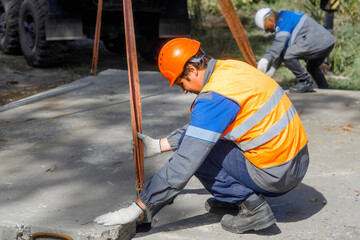Slinger lays concrete slab on construction site on summer day. Worker in protective vest and...