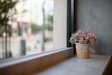view of colorful gypsophila flowers in paper pot on windowsill by window