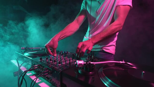 Nightclub DJ playing music on a party. Close up 4K video of cool young disc jocket mixing vinyl records on stage
