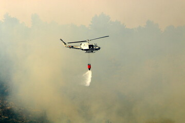Fototapeta na wymiar A helicopter puts out a forest fire in the mountains of northern Israel.