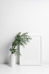 Picture frame mockup in white room with green eucalyptus in vase, blank frame mockup with copy space