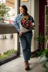 full length portrait of handsome brunette woman with flower bouquet staying by the window