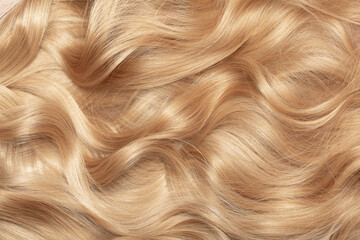 Blond hair close-up as a background. Women's long blonde hair. Beautifully styled wavy shiny curls. Hair coloring. Hairdressing procedures, extension.