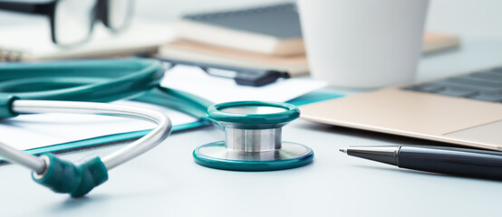 Green medical stethoscope closeup on doctor desk with pen and laptop