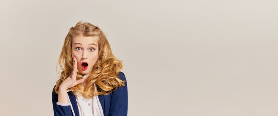 Wow, shock. Emotional young blonde woman with retro style hairdo wearing vintage outfit posing isolated over grey background. Emotions, facial expression concept