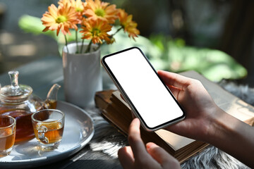Hands holding smart phone against traditional tea set with cups and teapot on rustic wooden table. Close up view