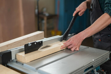 Close-up of a man cutting a wooden board on a sawing machine.