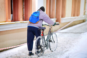 Old man with bicycle push bike on deep snow at city street after blizzard. Alone man with bicycle walking on snow covered road in cold winter day