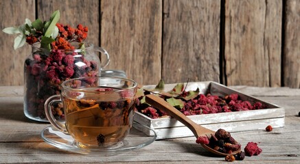 Wooden vintage background with a cup of fruit tea with dried berries of hawthorn, sea buckthorn,...