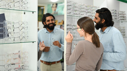 Smiling male optician helping caucasian woman choosing the most appropriate eyeglasses. Eyesight and vision concept