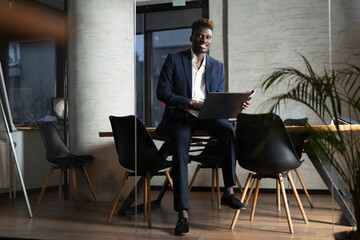 Portrait of successful businessman in office. Young smiling man using the laptop.