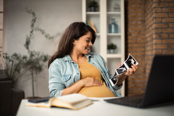 Beautiful young pregnant woman holding ultrasound pictures of her baby. Businesswoman having video call