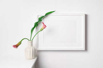 Horizontal picture frame mockup on white wall with flowers, blank frame with copy space