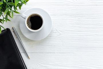 Office table with cup of hot black coffee and notebook