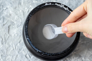 female hand takes a measuring spoonful of BCAA powder from a large black jar. Close-up. Protein for...