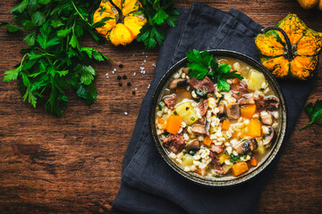 Winter comfort food. Warming soup with pumpkin, mushrooms, vegetables, beef and barley. Rustic wooden table background, top view