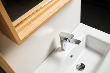 Fototapeta premium Interior of bathroom with washbasin mirror cabinet over the sink and faucet modern loft flat minimalistic design with modern countertop basin, illuminated mirror and wooden PVC cupboard.