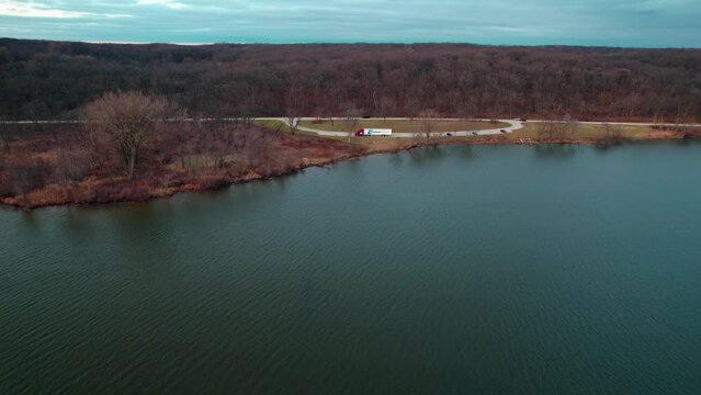 cinematic aerial of a red semi truck and white trailer parked on side of a lake. Autumn 2022. Location: saganashkee slough woods, willow springs Illinois, usa.