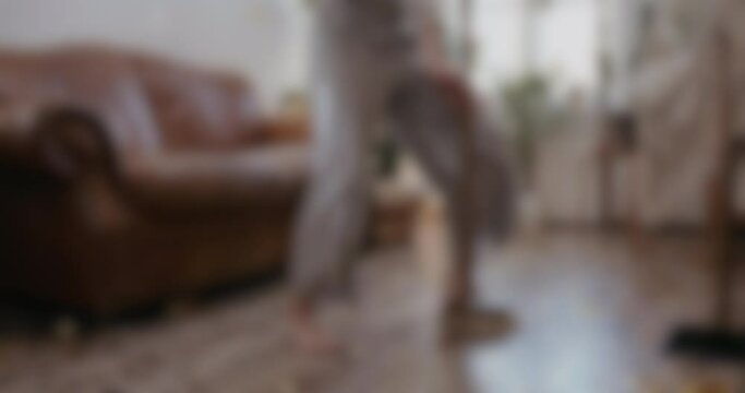 Blurred shot of woman dancing while cleaning the house with a broom, having fun while doing domestic household maintenance.