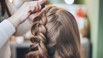Fototapeta premium The girl makeup artist makes a braid for the model.