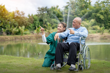 beautiful nurse takes care of an elderly man in a wheelchair laughing on the bridge by the pond in the park.