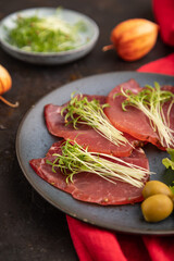 Slices of smoked salted meat with cilantro microgreen on black. Side view, selective focus.